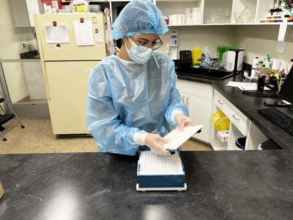 A-professional-woman-in-a-lab-coat-and-glasses-holds-a-box-representing-Butterfields Compounding Pharmacy & Medical supplies.